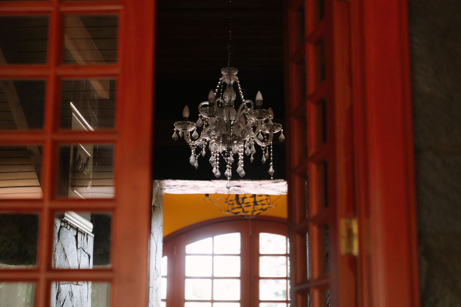 Elegant crystal chandelier hanging between red wooden doors in a rustic wedding venue interior.