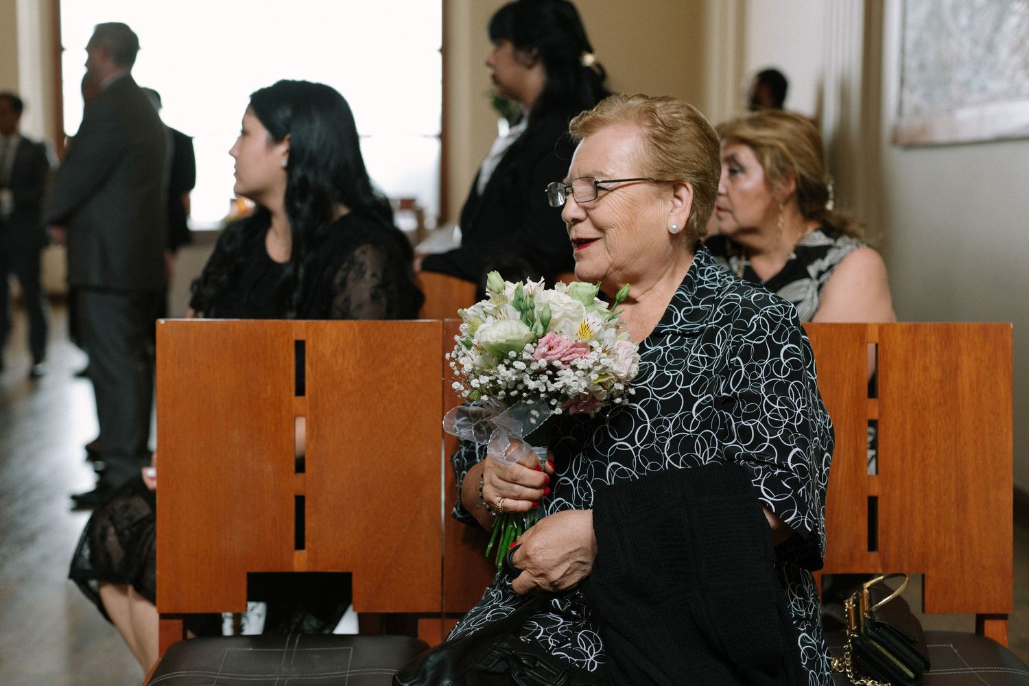 Guest holding floral bouquet while seated in wooden chairs at formal event.
