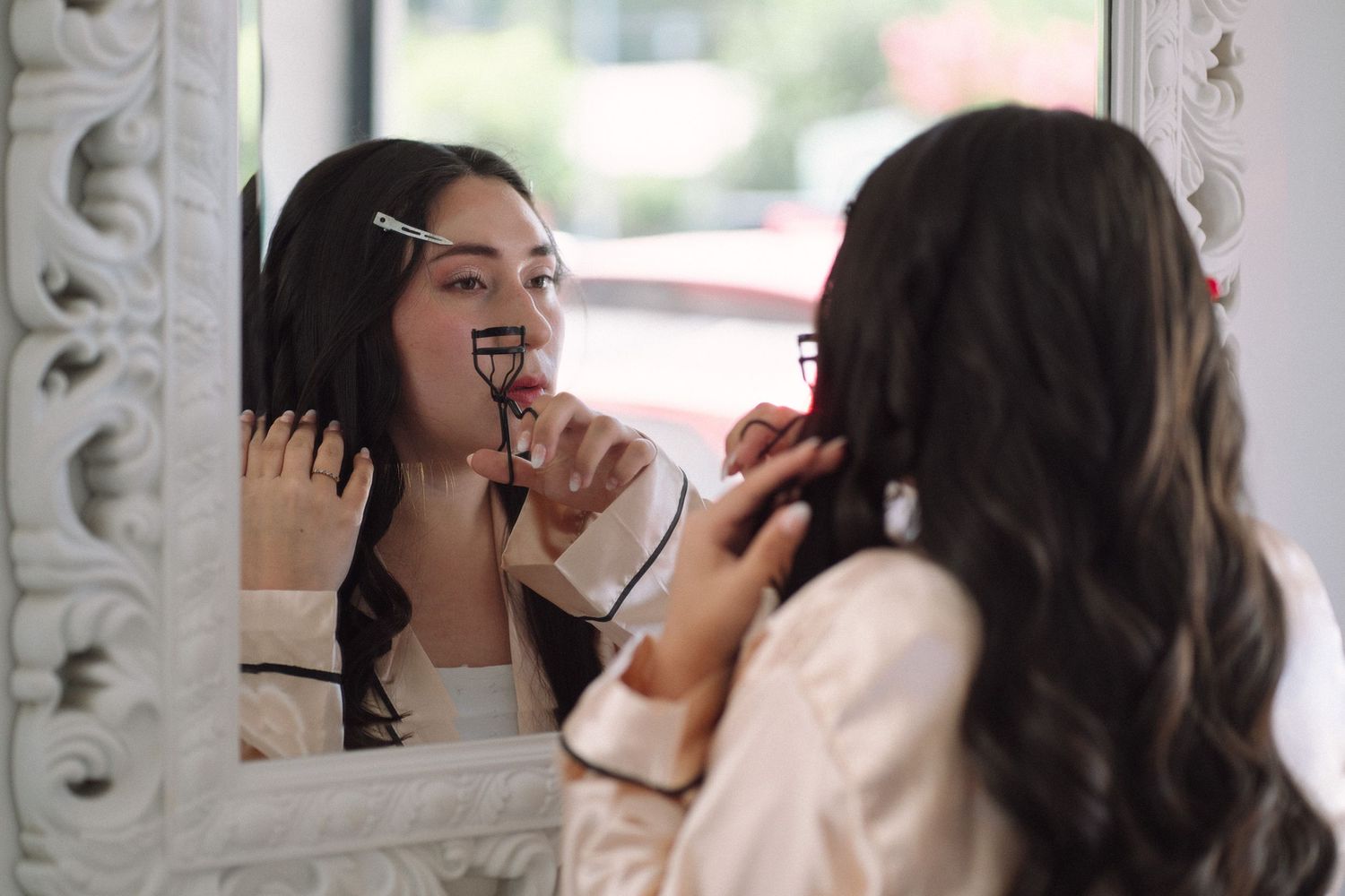Person looking into an ornate mirror while applying makeup and smiling.
