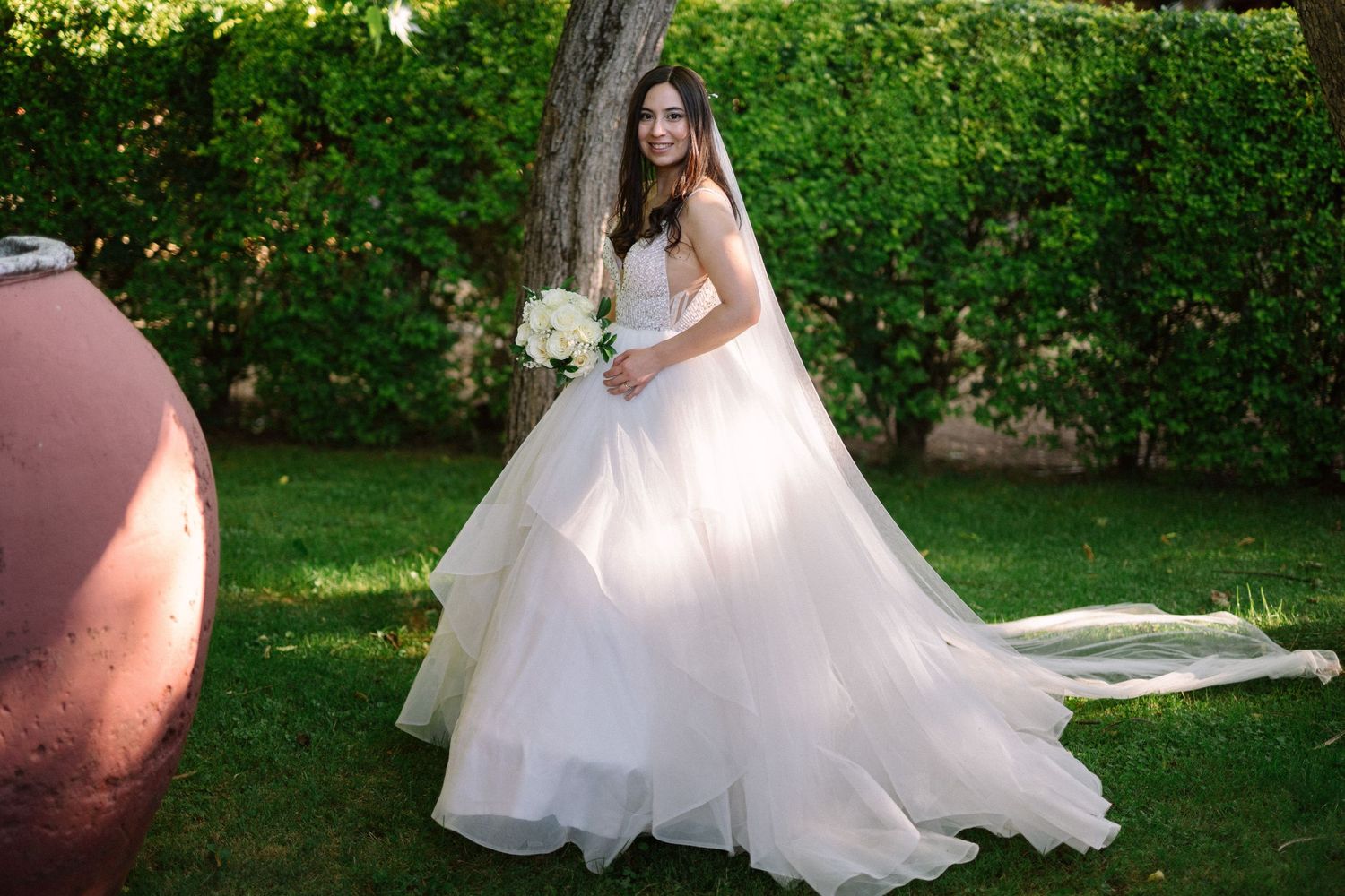 Person in flowing white wedding dress poses with bouquet in garden setting.
