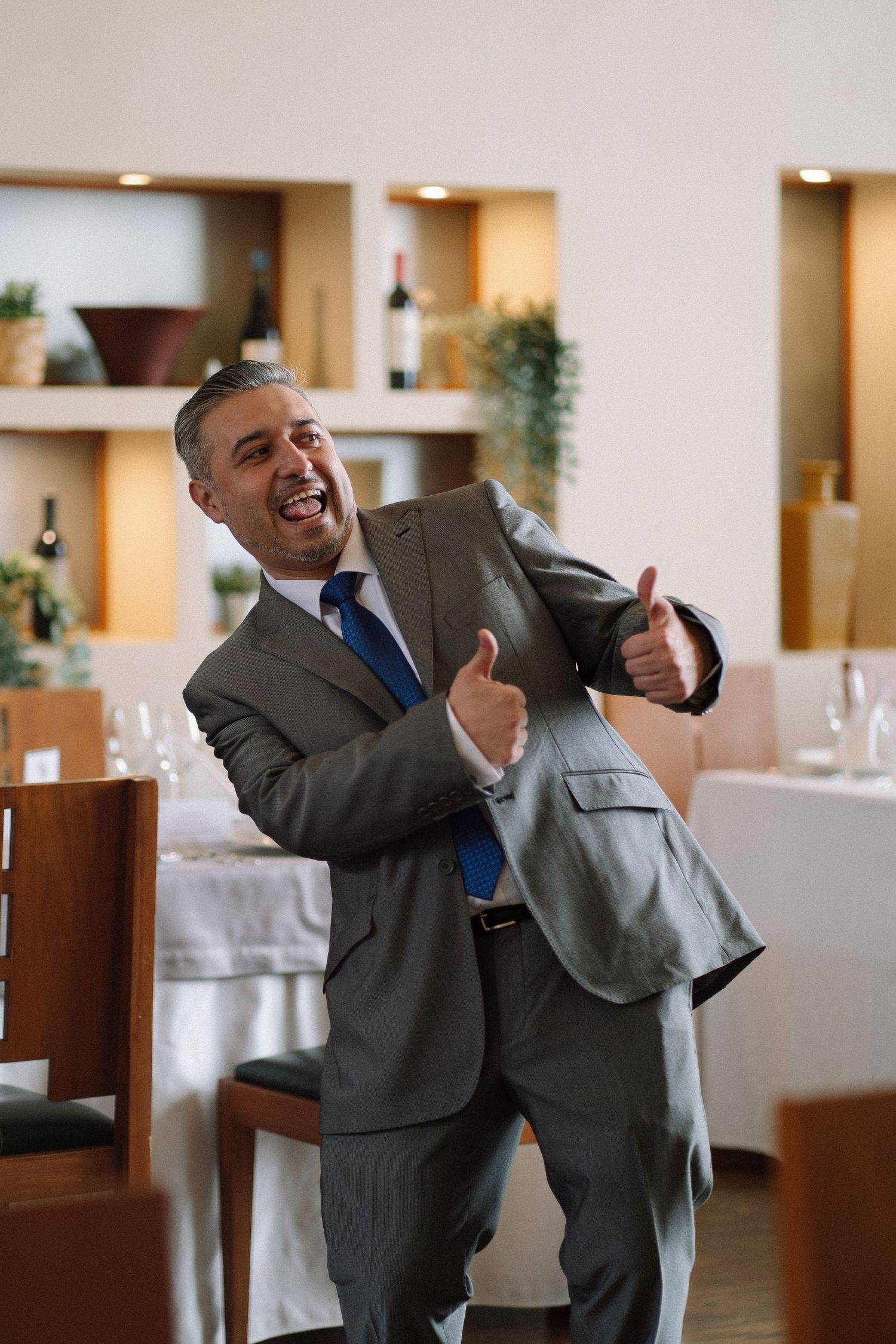 A person in a gray suit expressing joy and laughter in a restaurant setting.