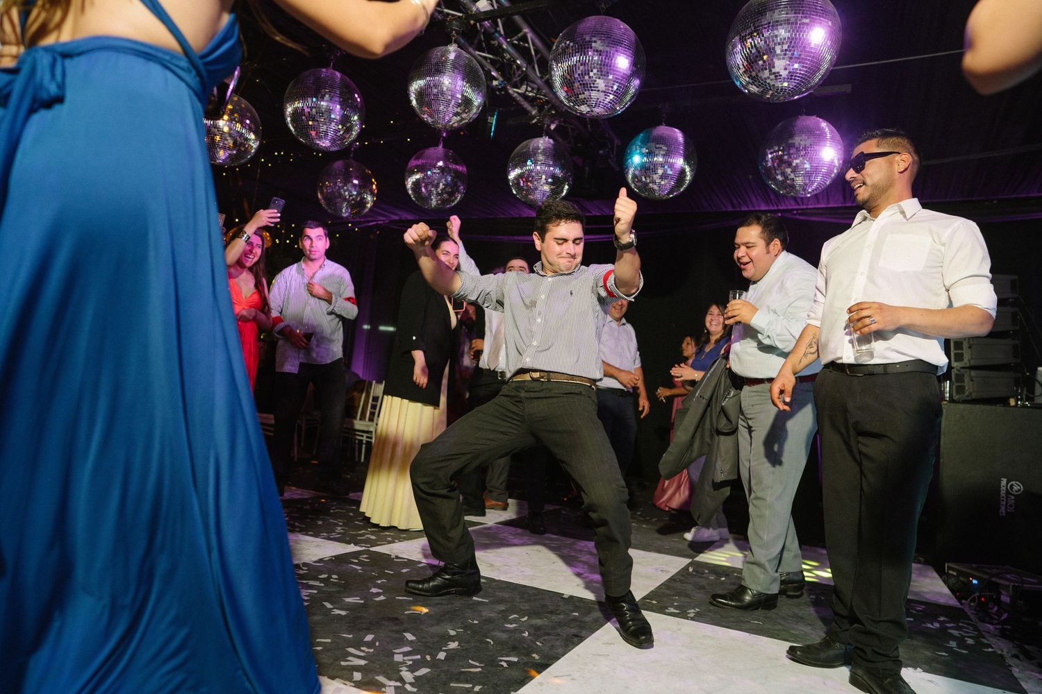 Wedding guests dancing under disco balls on a checkered dance floor during a lively celebration.