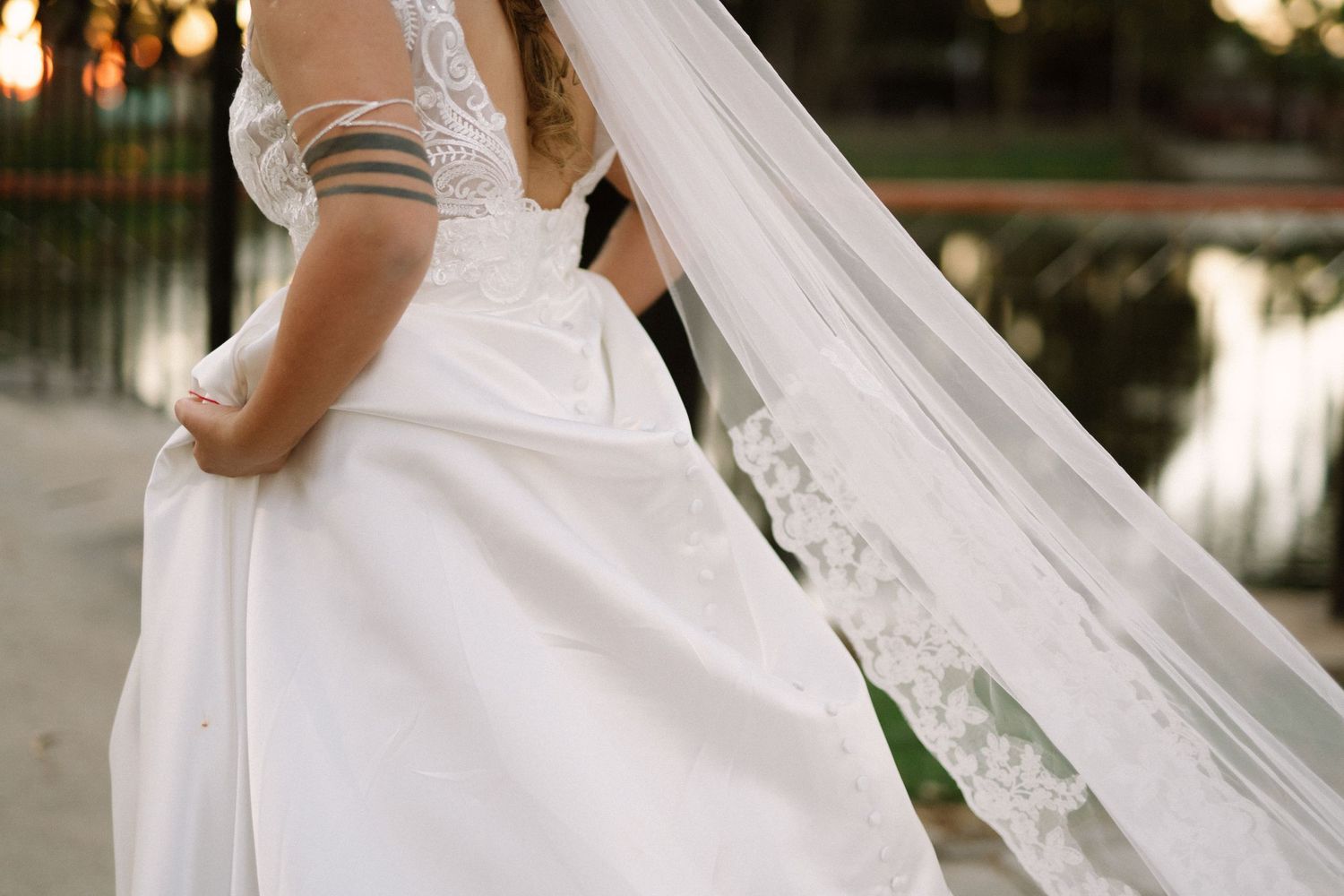 Detail shot of a flowing white wedding dress with lace details and long veil trailing behind.