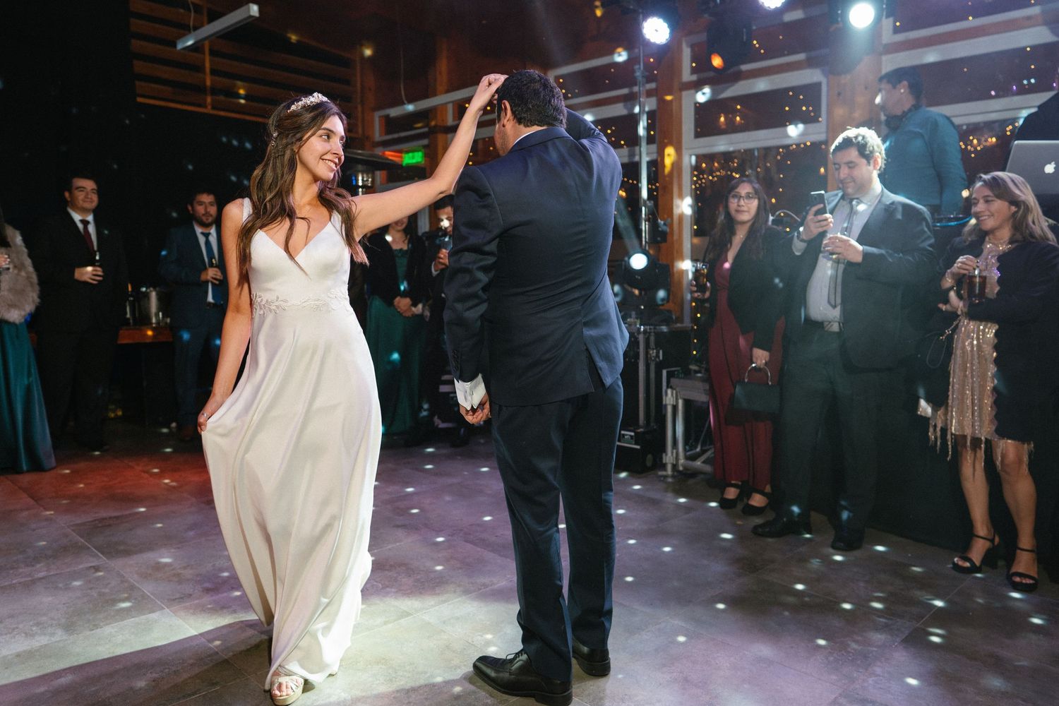 Wedding couple dancing surrounded by guests under bright stage lighting and falling confetti.