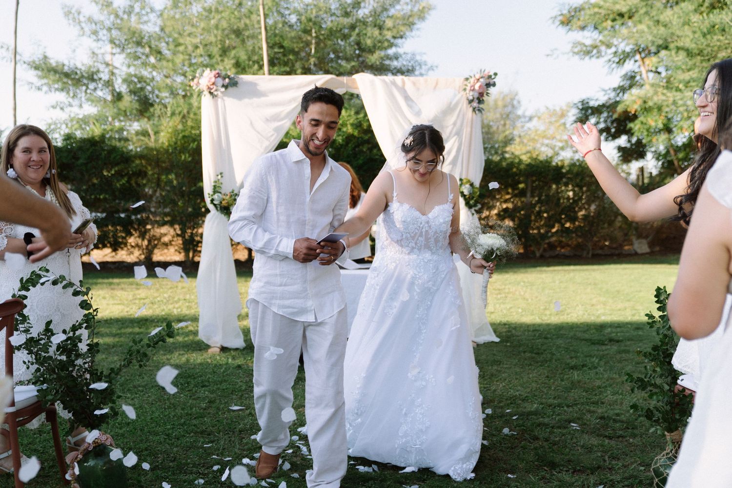Joyful newlyweds walk hand-in-hand down the aisle after outdoor wedding ceremony as guests celebrate.