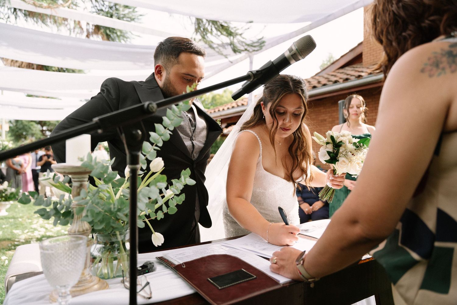 Bride signing the marriage certificate at the altar with the groom smiling beside her.