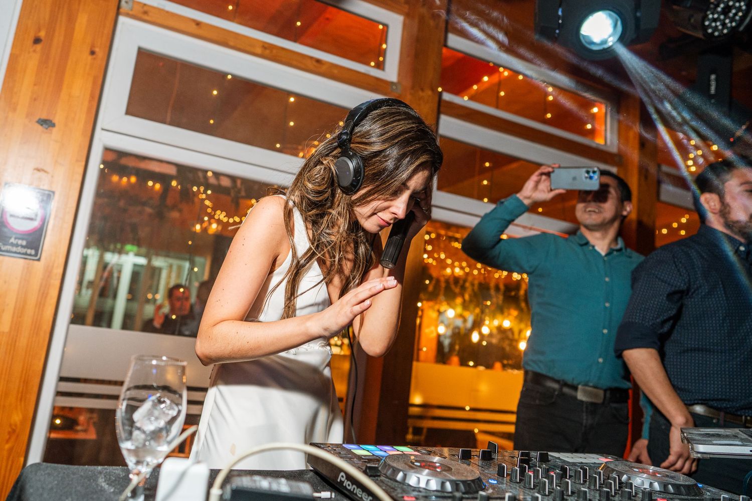 Energetic dancing and celebration at a DJ booth with wooden decor and string lights.