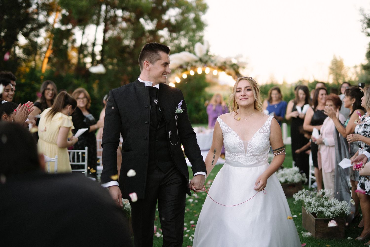 A joyful wedding couple walking down the flower-lined aisle as guests look on.