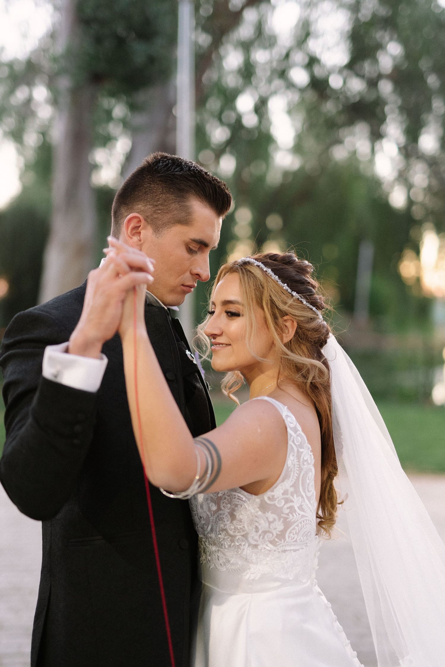 A wedding couple dances together on a stone path surrounded by trees at sunset.