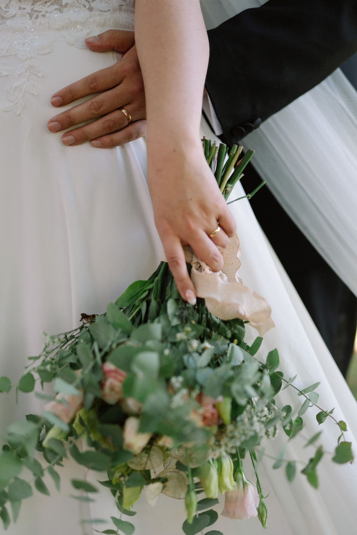 Wedding bouquet showcasing eucalyptus and blush roses held by hands wearing white dress and engagement ring.