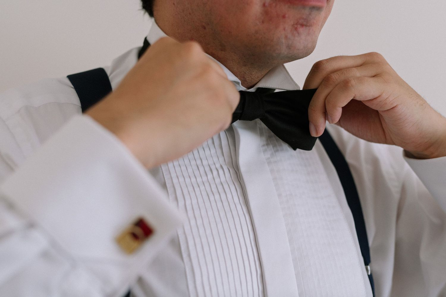 Close-up detail of hands adjusting formal black bow tie on white dress shirt.