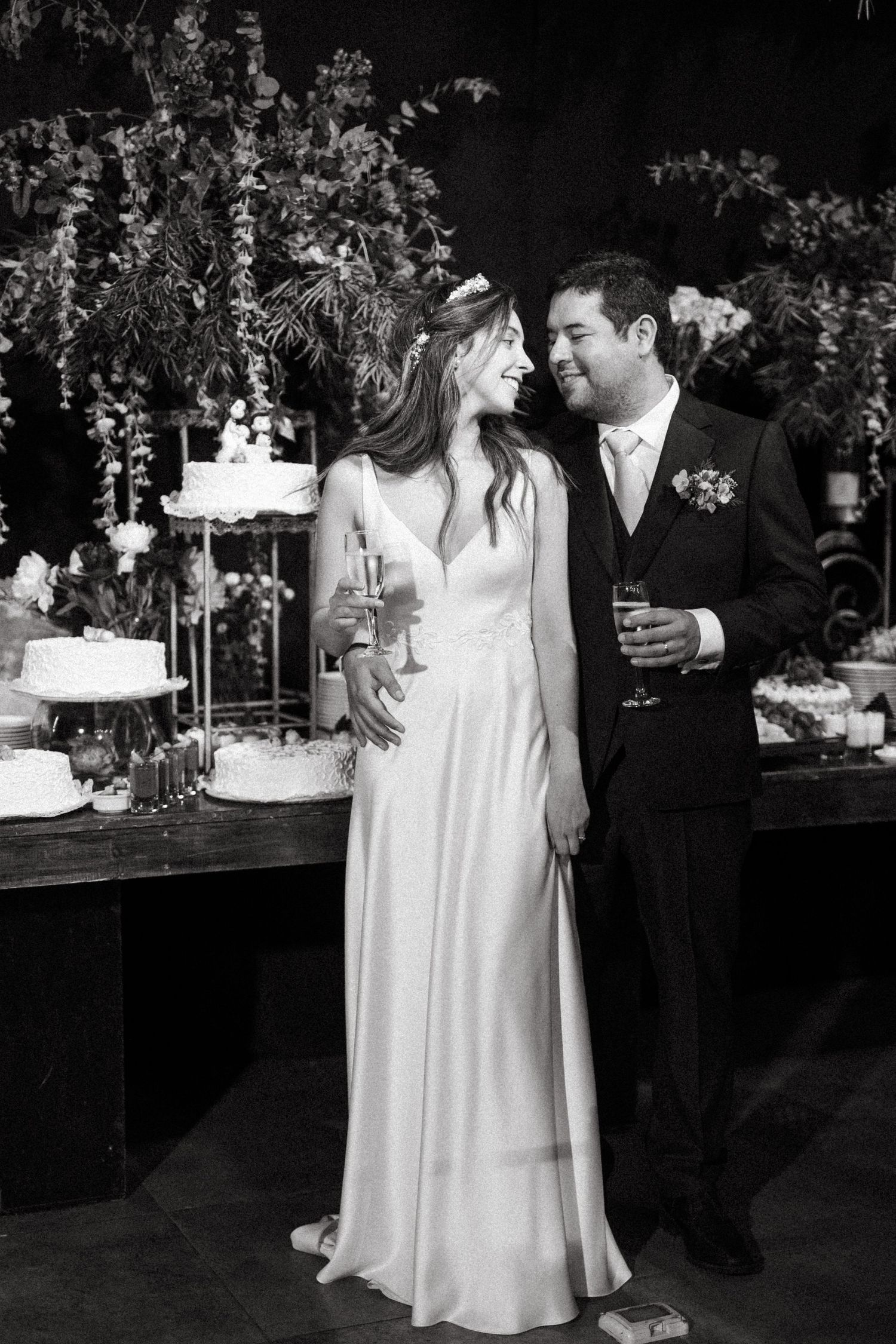 Black and white wedding reception photo with couple smiling by tiered cake display with romantic decor.