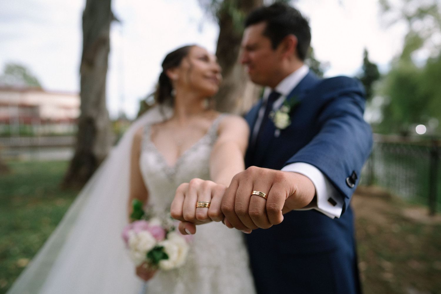 Wedding couple showing off their rings in an intimate moment outdoors.