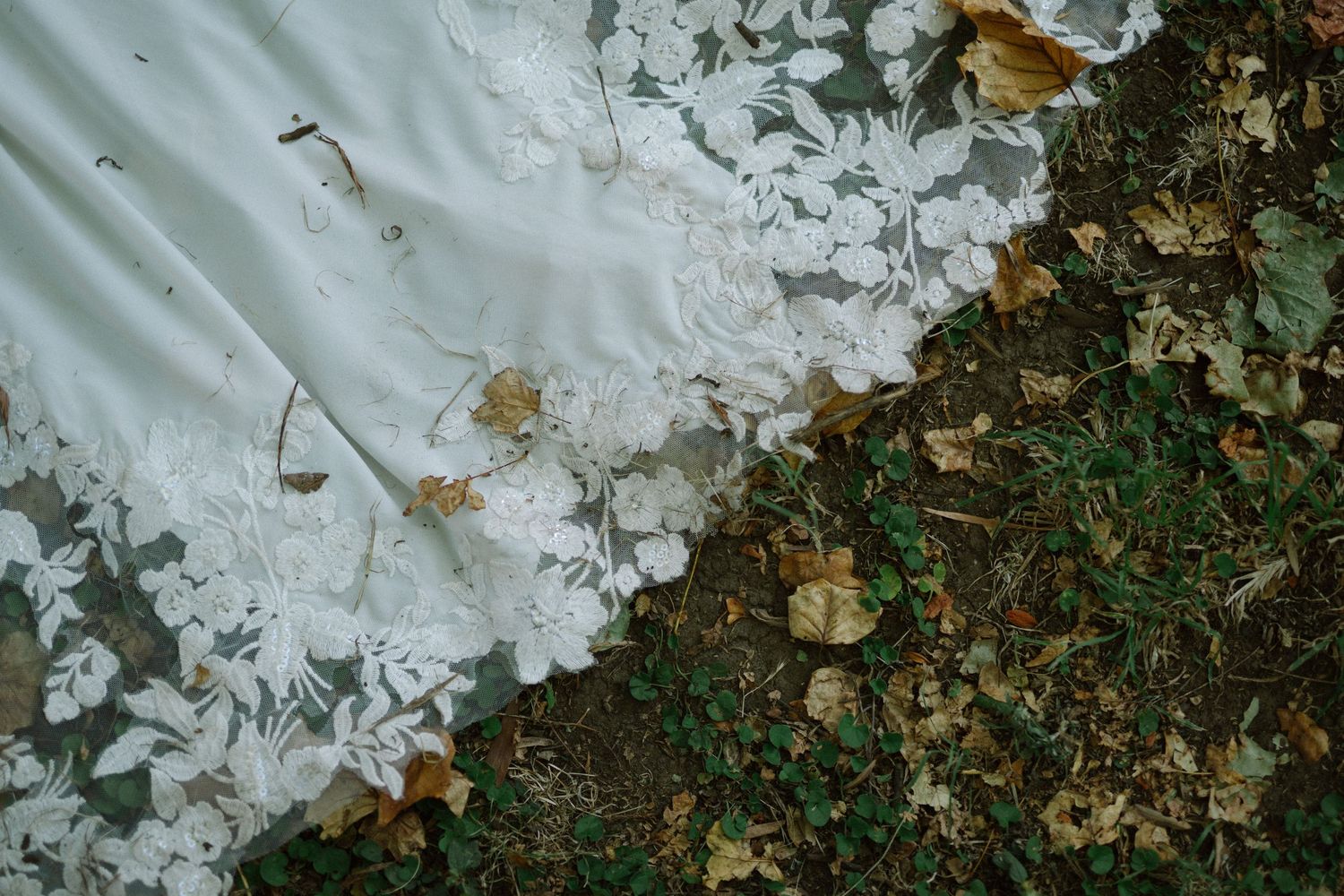 White wedding dress hem trailing over fallen autumn leaves on the ground.