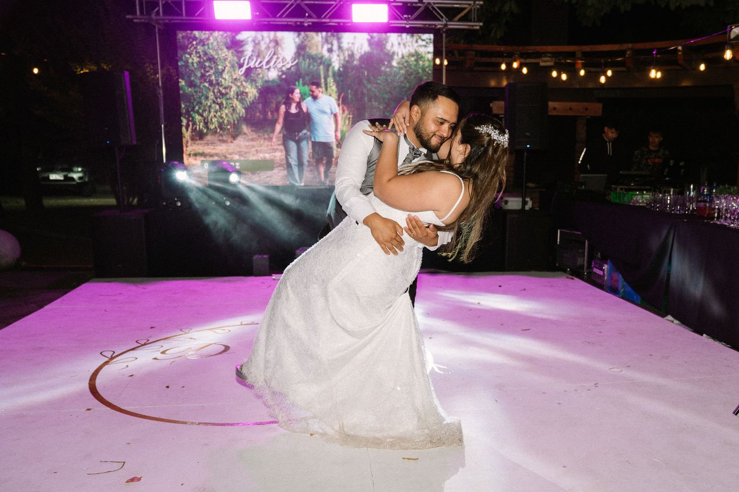 Groom dipping bride during romantic first dance on illuminated white wedding dance floor.
