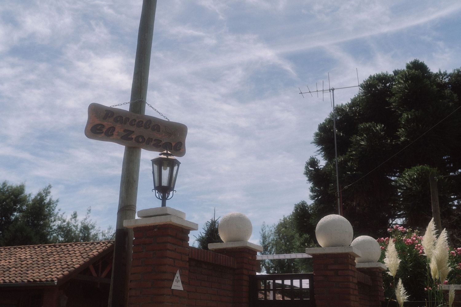 Brick entrance gate with globe lights and lantern street lamp at an outdoor wedding venue under cloudy sky.
