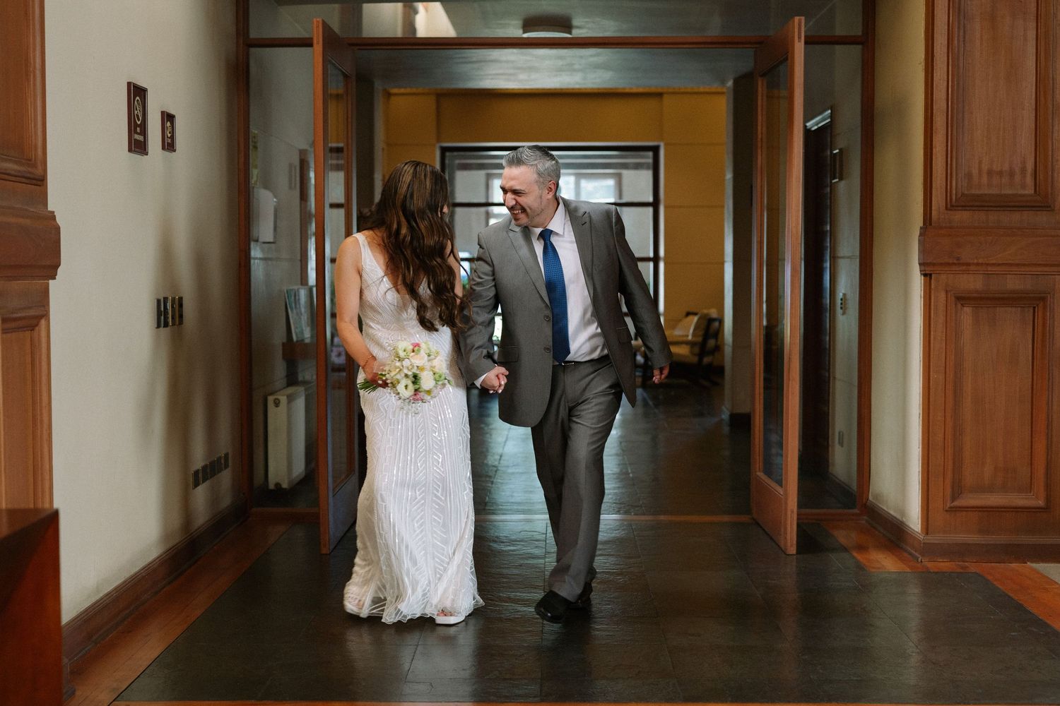 Newlyweds walking down a vintage hallway with warm lighting.