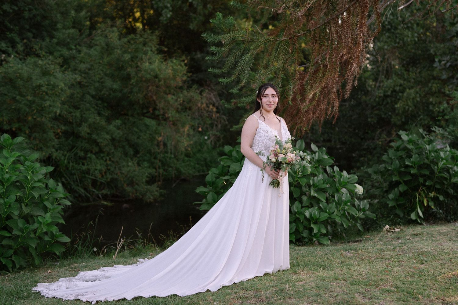 An elegant bridal portrait in a garden featuring a long-trained white wedding gown.
