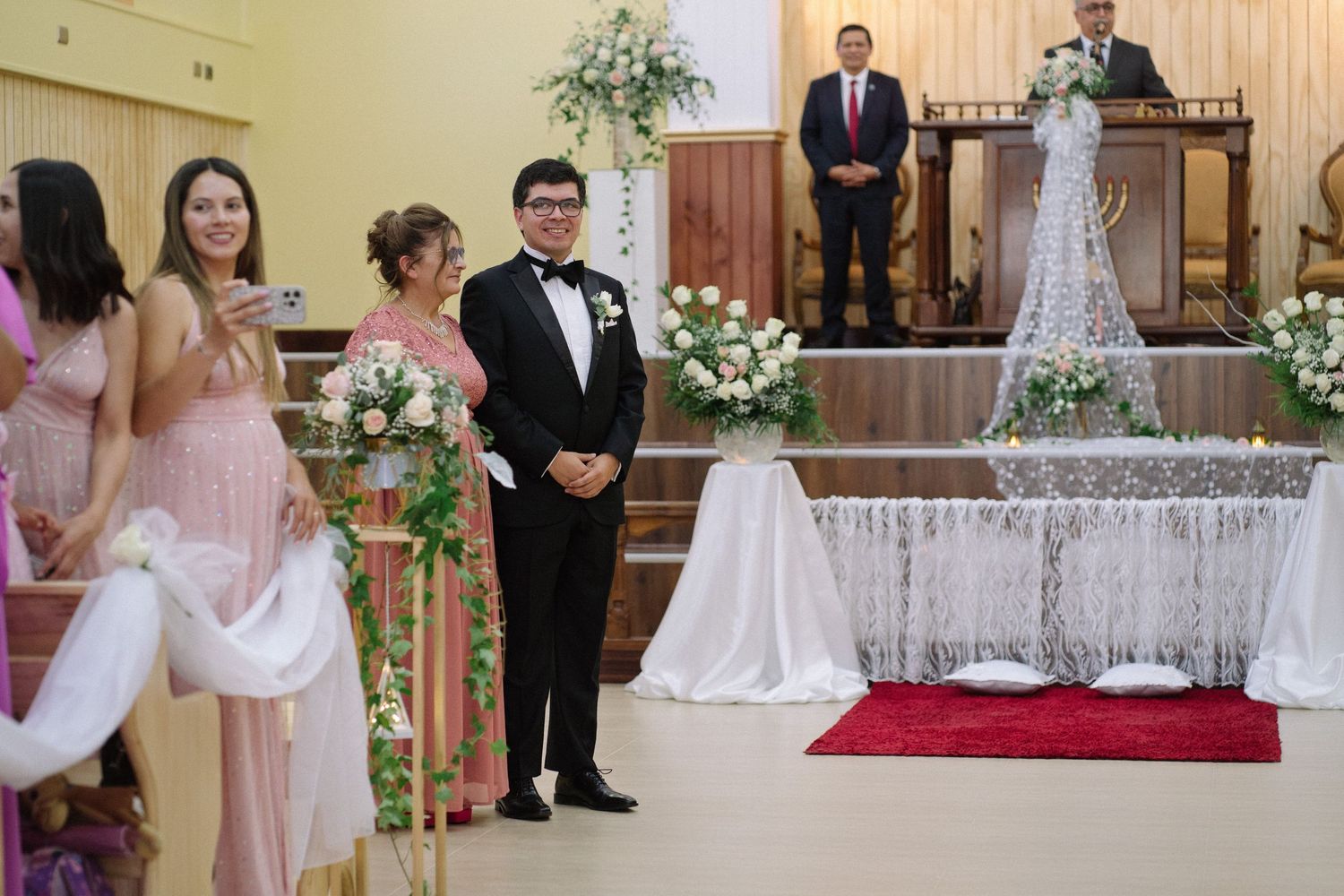 A wedding ceremony setup in a church with floral decorations and a red carpet leading to the altar.