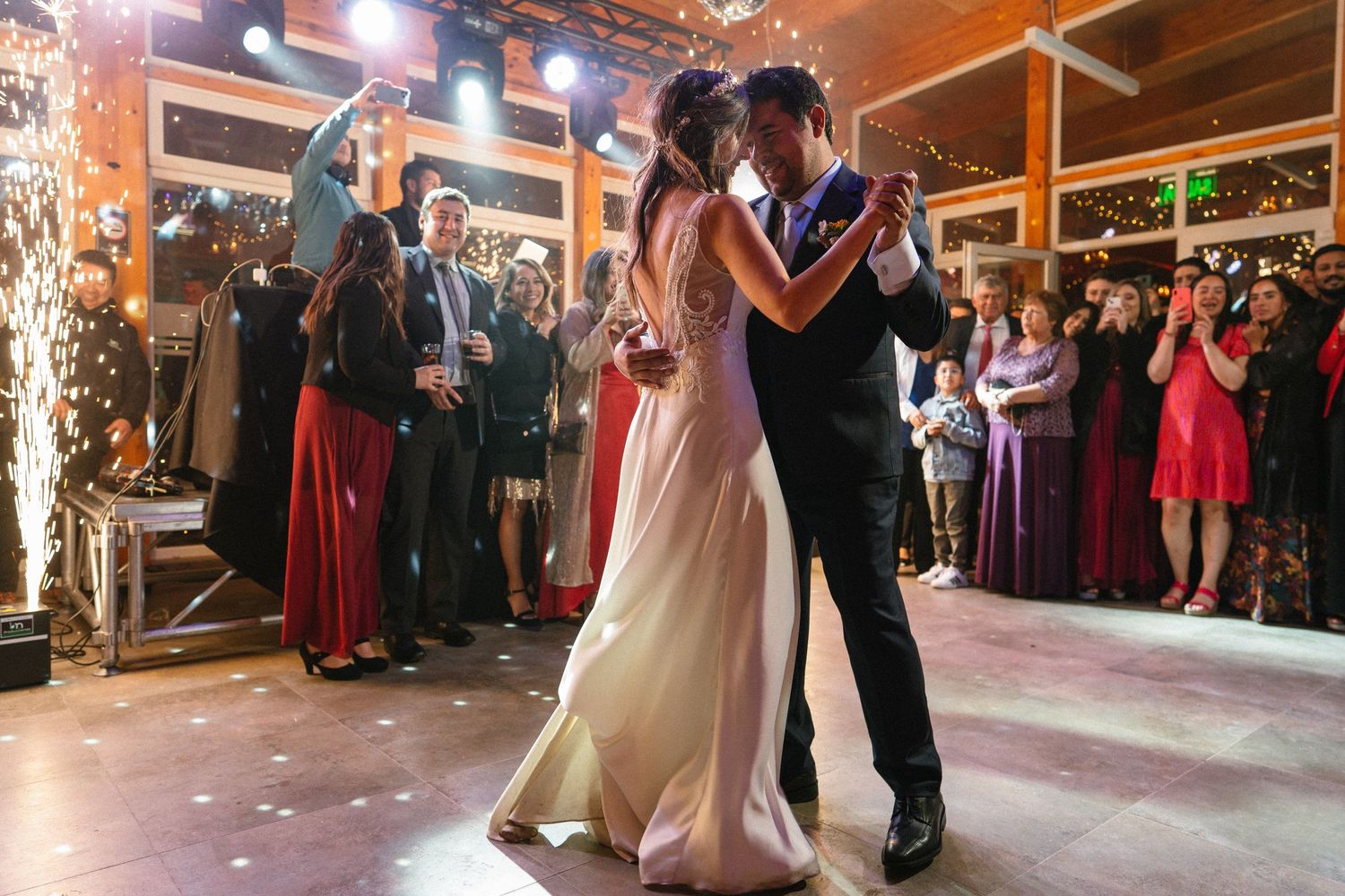 A couple slow dances on an illuminated dance floor while wedding guests look on.