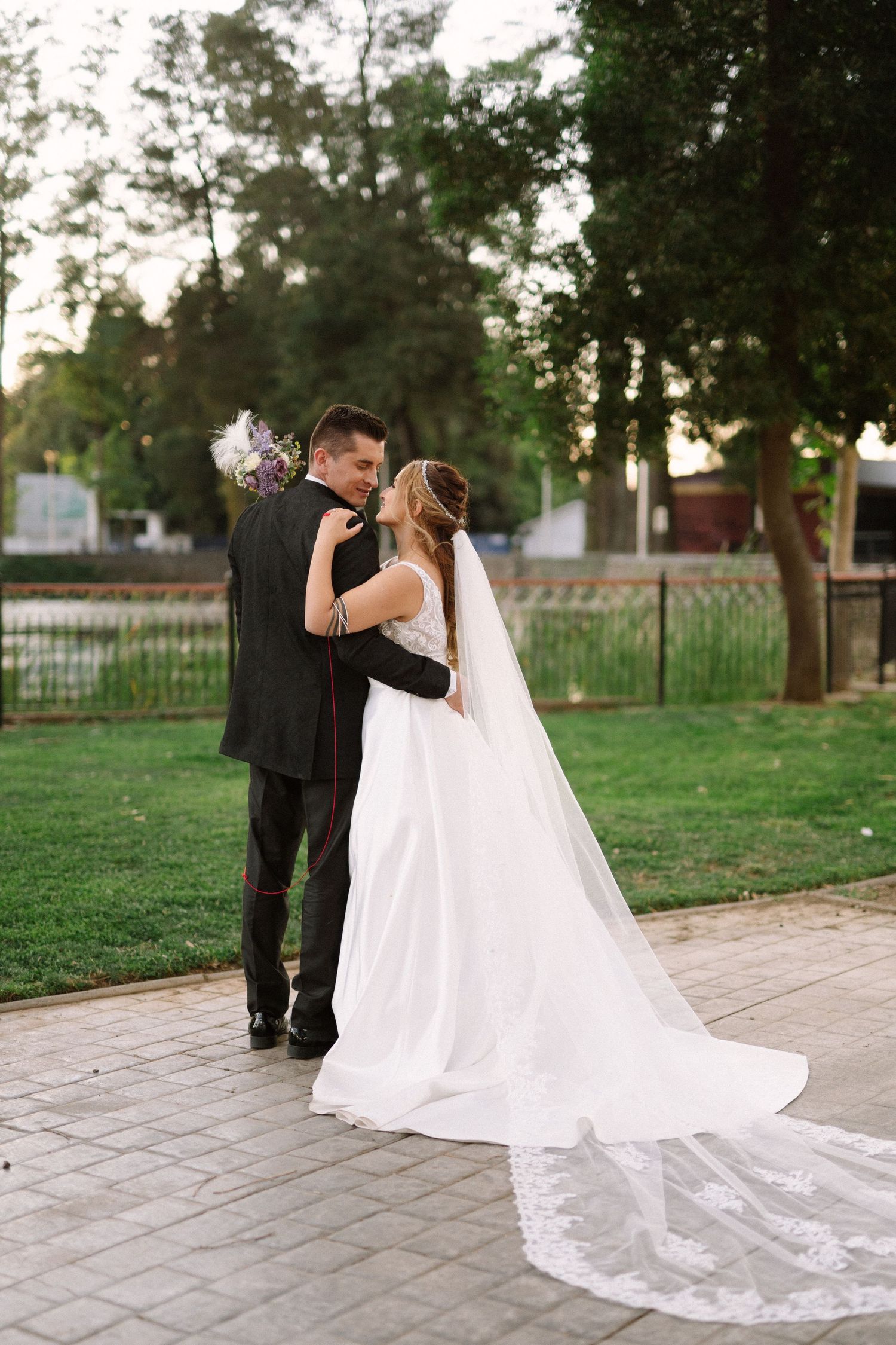 A tender wedding moment photographed in a park with tall trees and evening light.