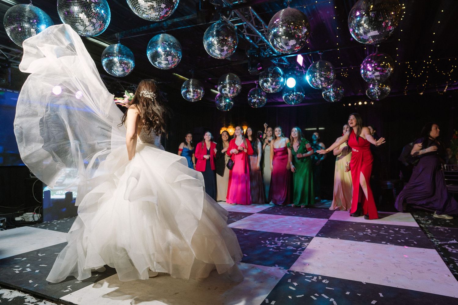 A flowing white wedding dress twirls on a checkered dance floor under hanging disco balls.