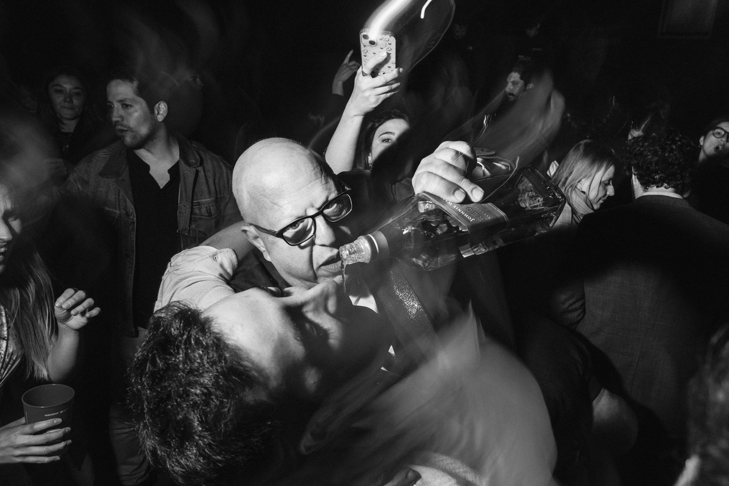 A black and white photo captures energetic dancing at a lively wedding reception.