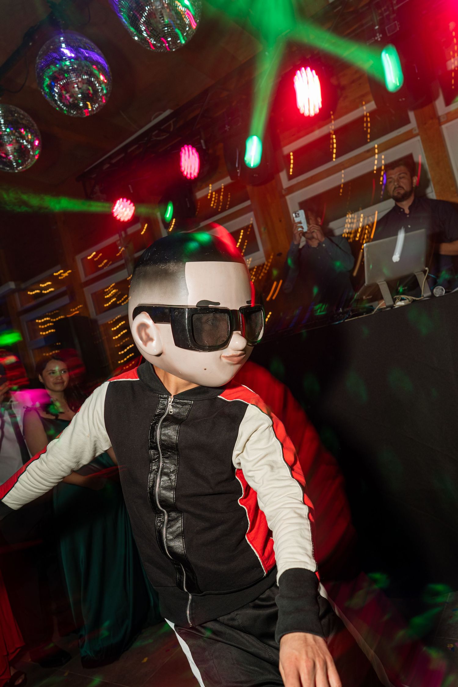 Dancer in white mask and two-tone outfit performing under disco lights.