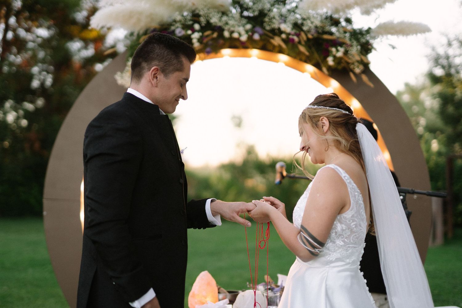 Intimate wedding ceremony moment captured under a lit circular arch with floral decorations.