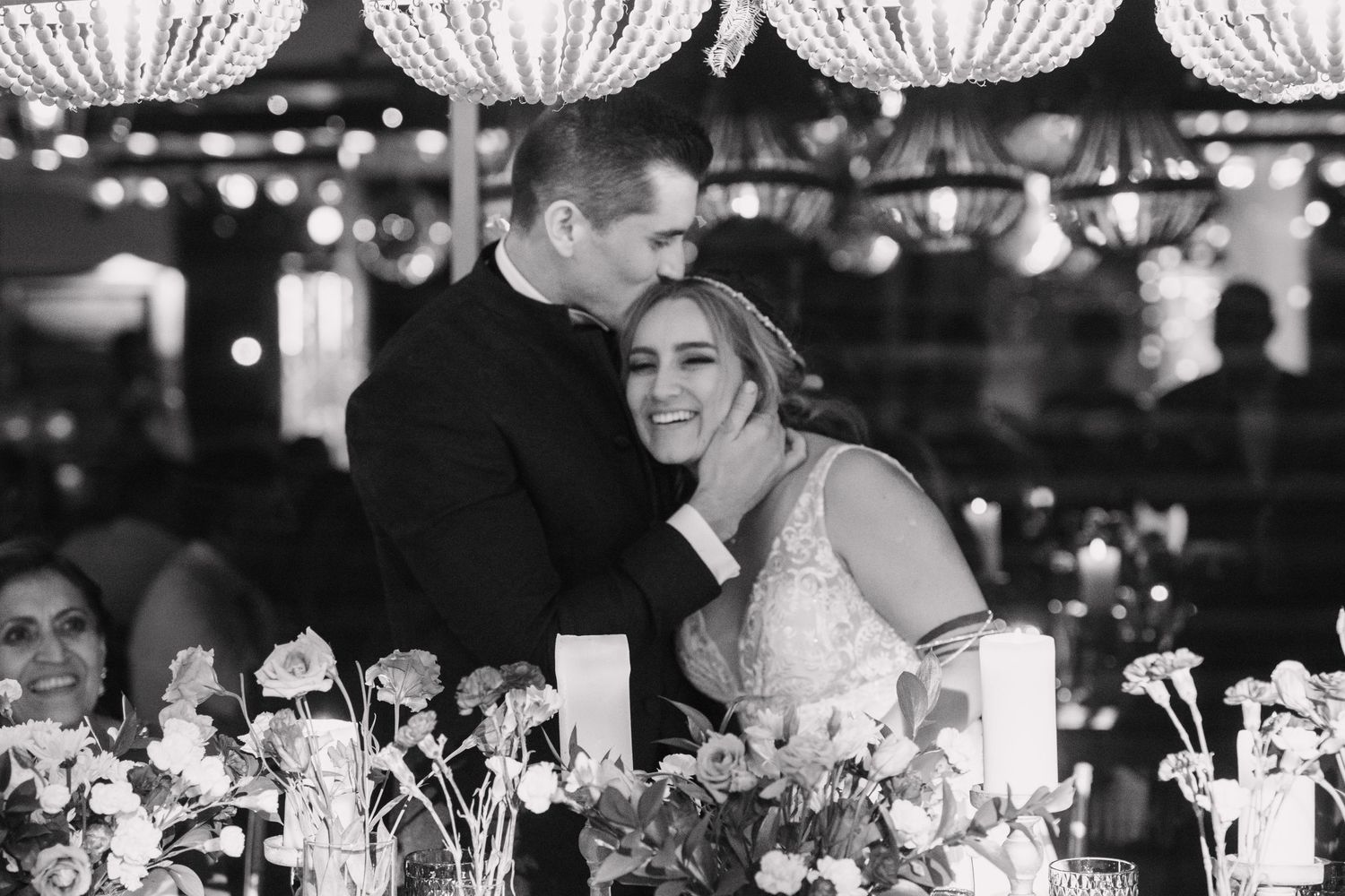 Black and white wedding reception photograph under crystal chandeliers with floral centerpieces.