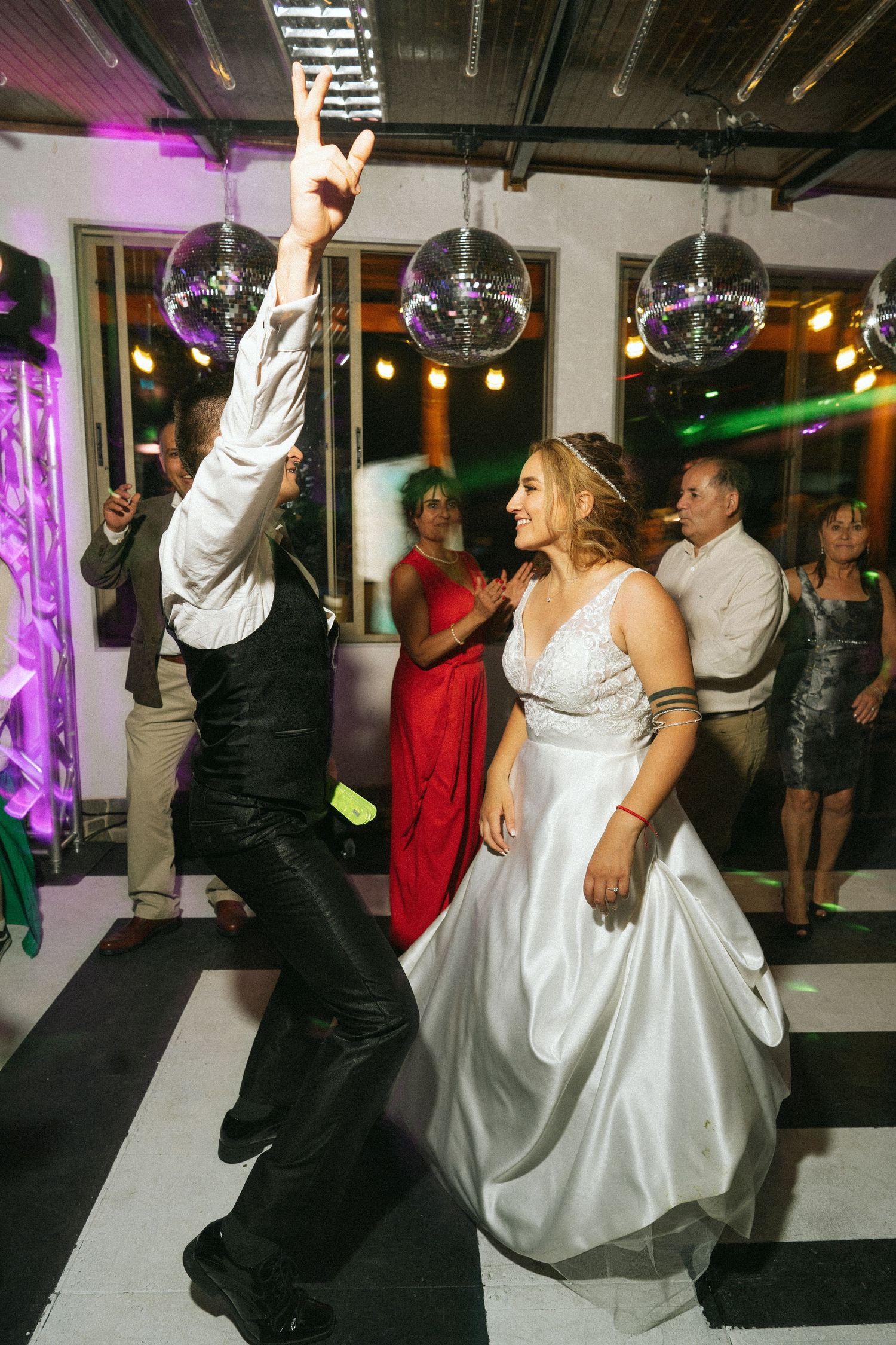 A bride and guest dancing energetically under disco balls at a wedding reception.