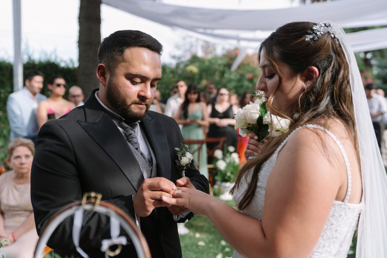 Groom placing wedding ring on brides finger during emotional outdoor ring exchange ceremony.