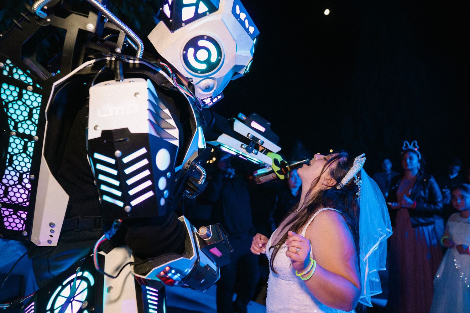 Bride interacting with impressive illuminated robot costume performer at nighttime wedding reception.