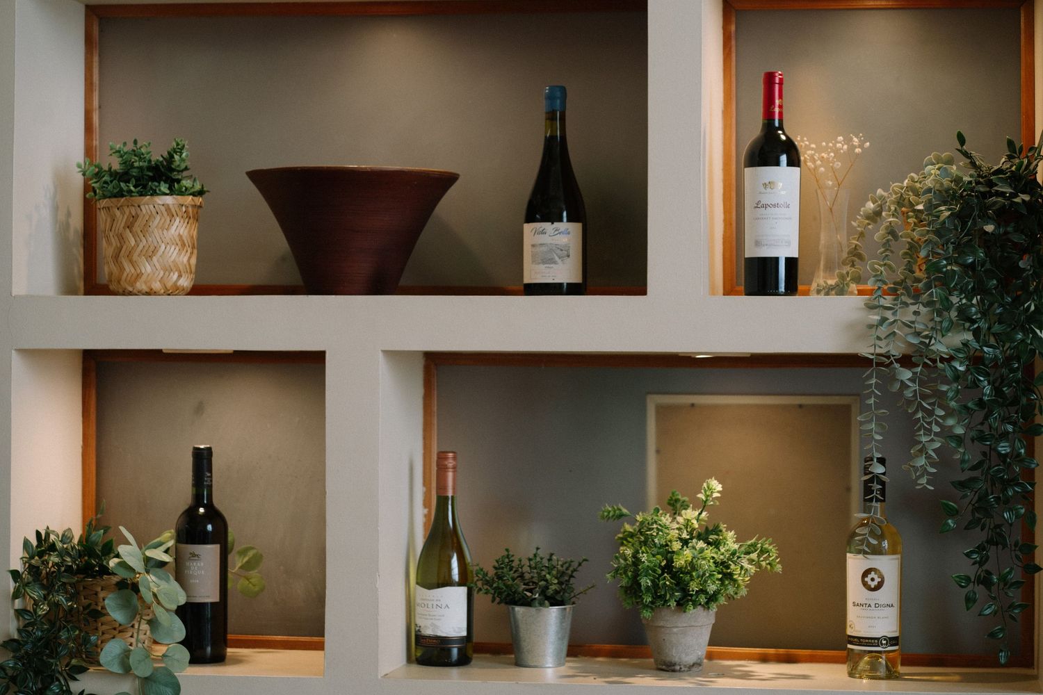 Wine bottles and potted plants displayed on built-in wall shelves in a restaurant or dining room.