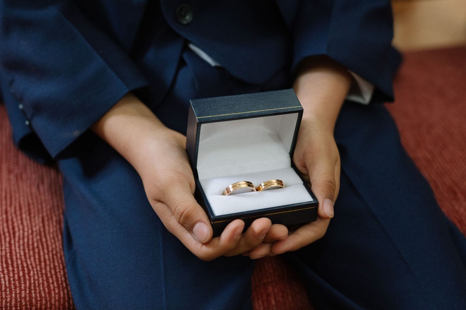 Hands holding open navy blue ring box with wedding bands inside.