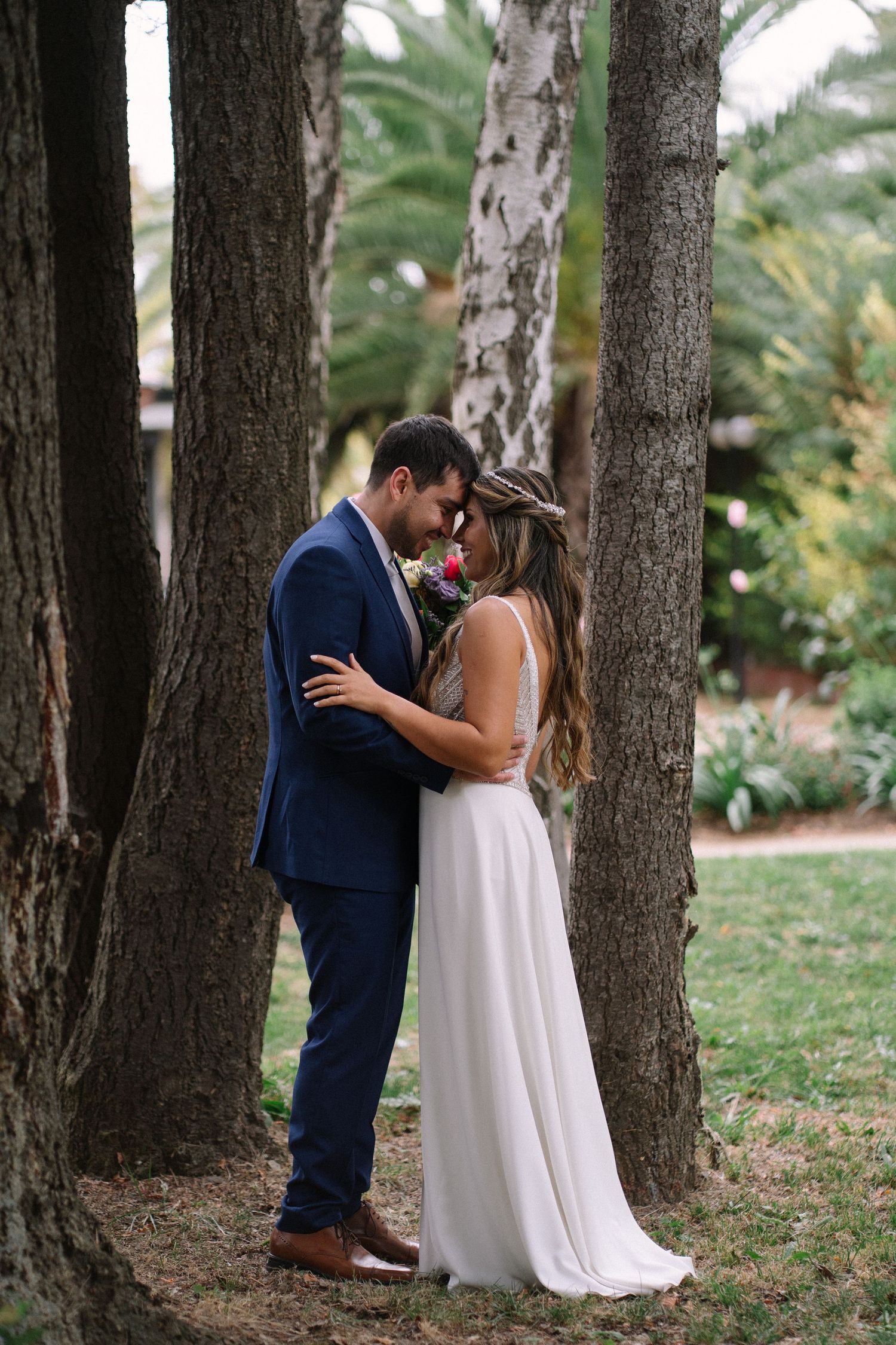 Wedding couple shares intimate moments among tall pine trees in an outdoor setting.