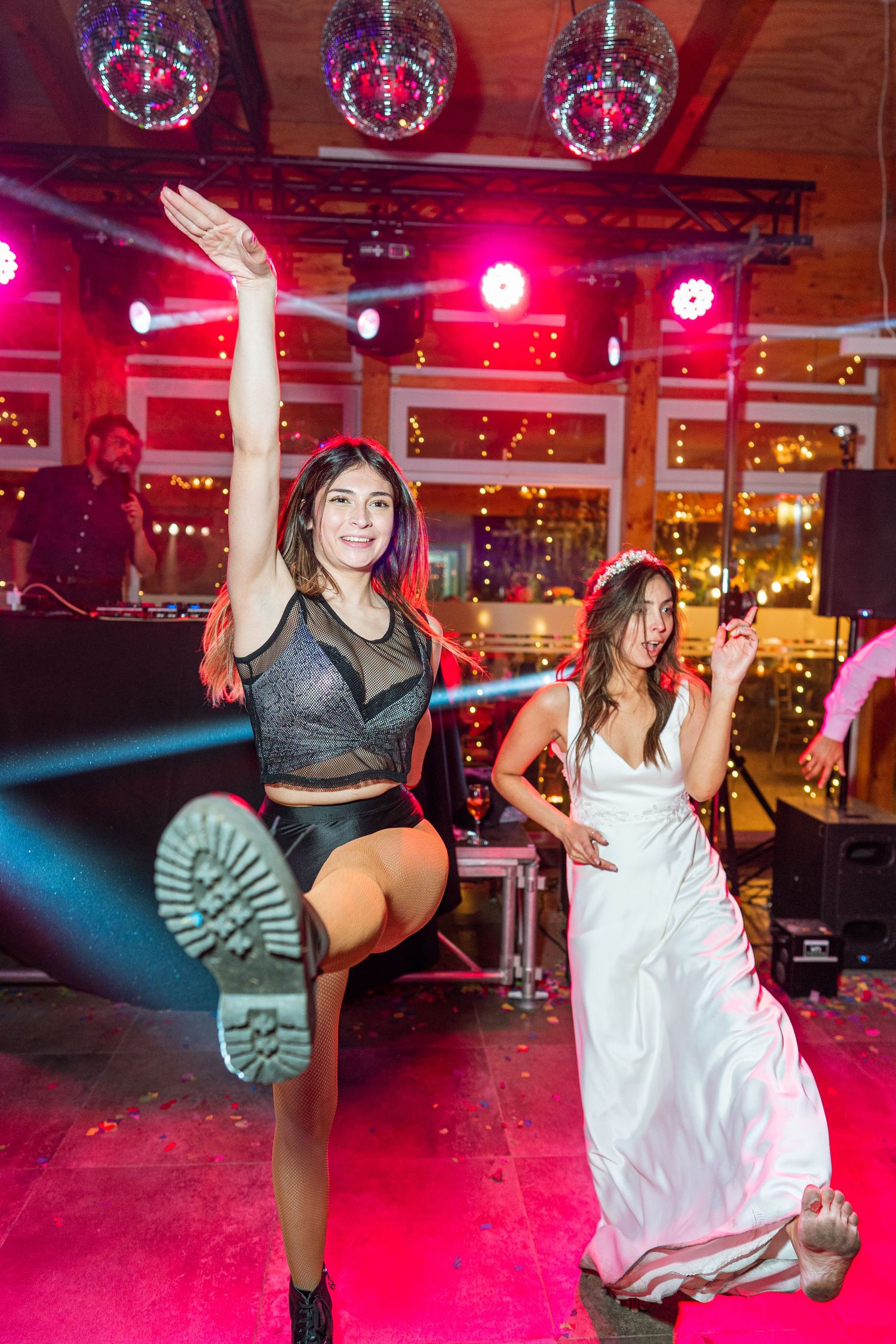 Dancers in a nightclub under red lighting as one performs an energetic leg kick during a celebration.