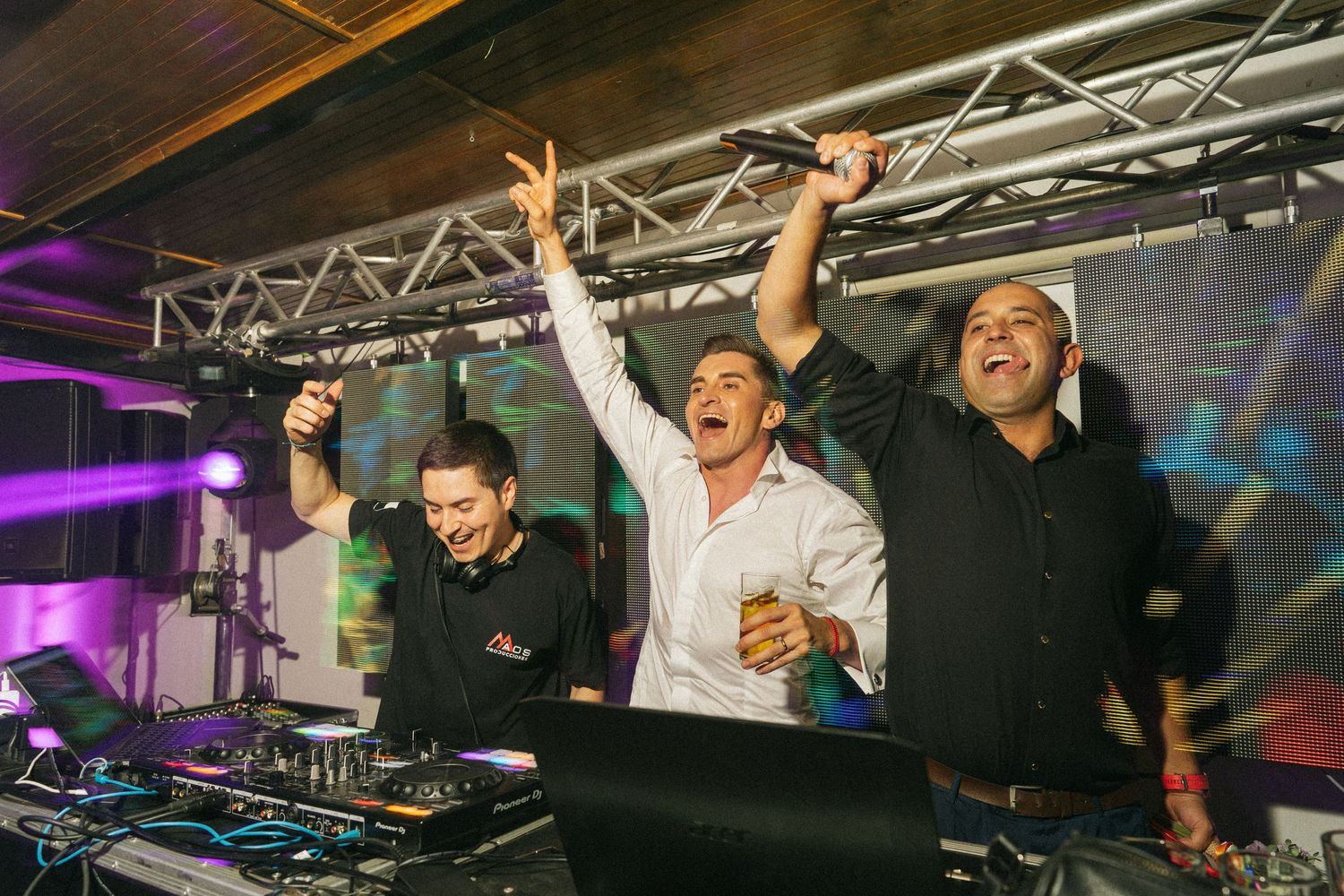 Three DJs celebrating behind the booth with raised arms at a party.