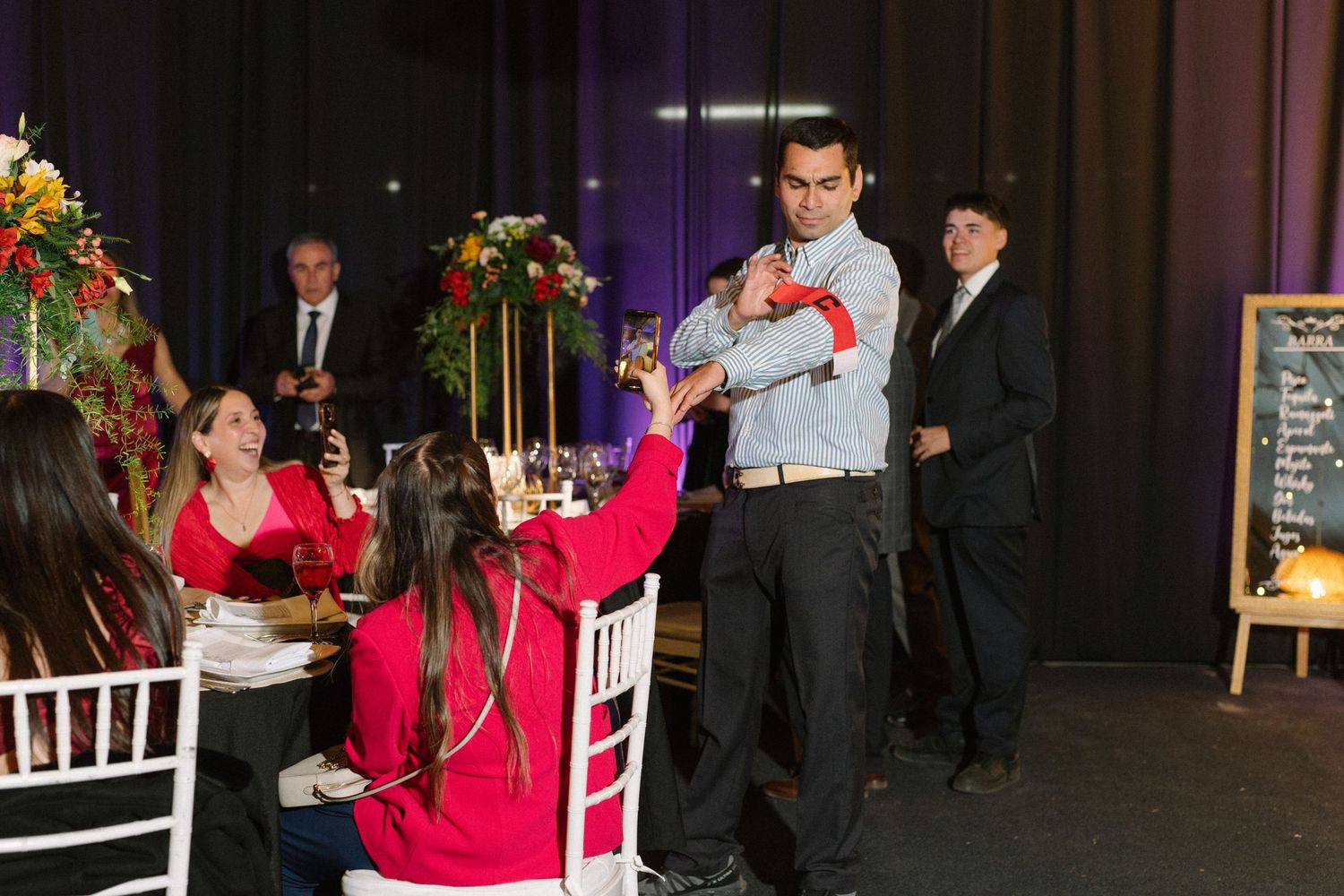 Wedding reception guests enjoying entertainment and floral centerpieces at decorated indoor venue.