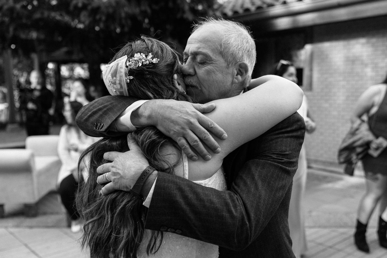 Emotional black and white photo of older man hugging bride at wedding celebration.
