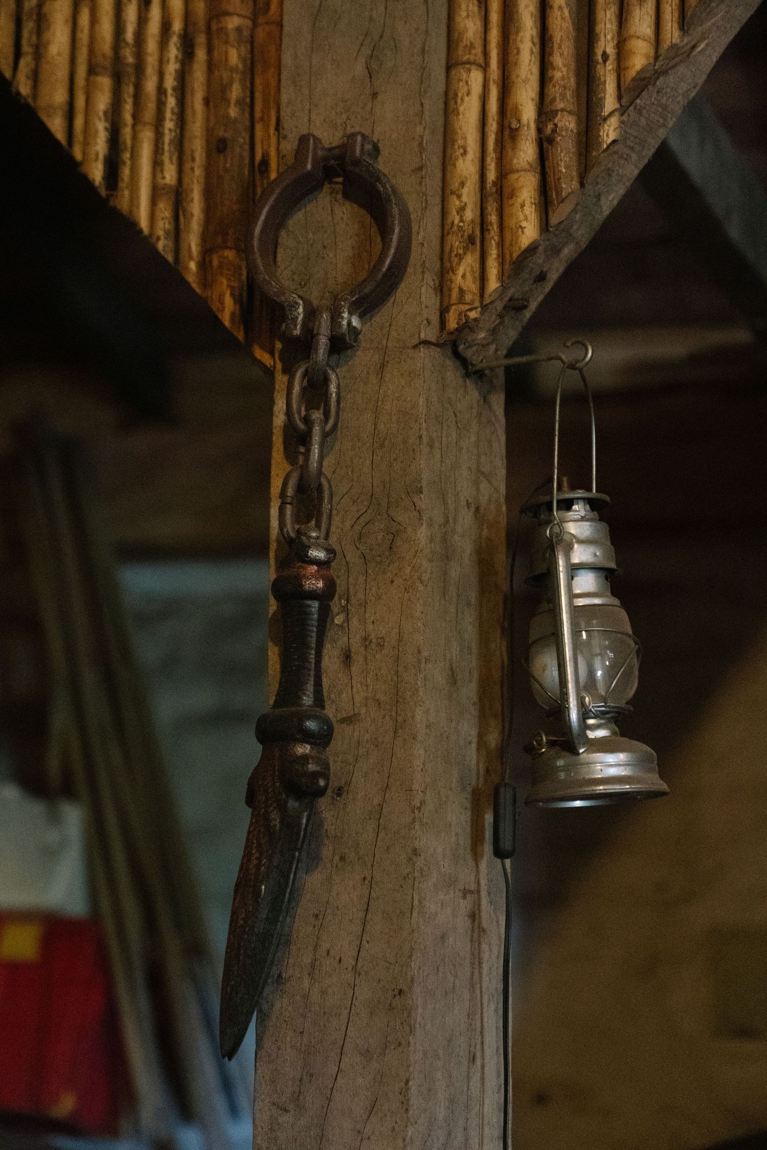 Rustic wooden post with vintage iron shackle chain and antique kerosene lantern hanging in old barn.