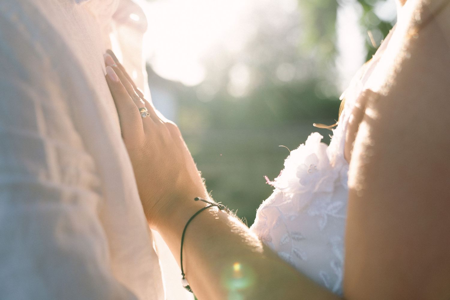 Close-up of bride and groom holding hands with golden sunlight at outdoor wedding.