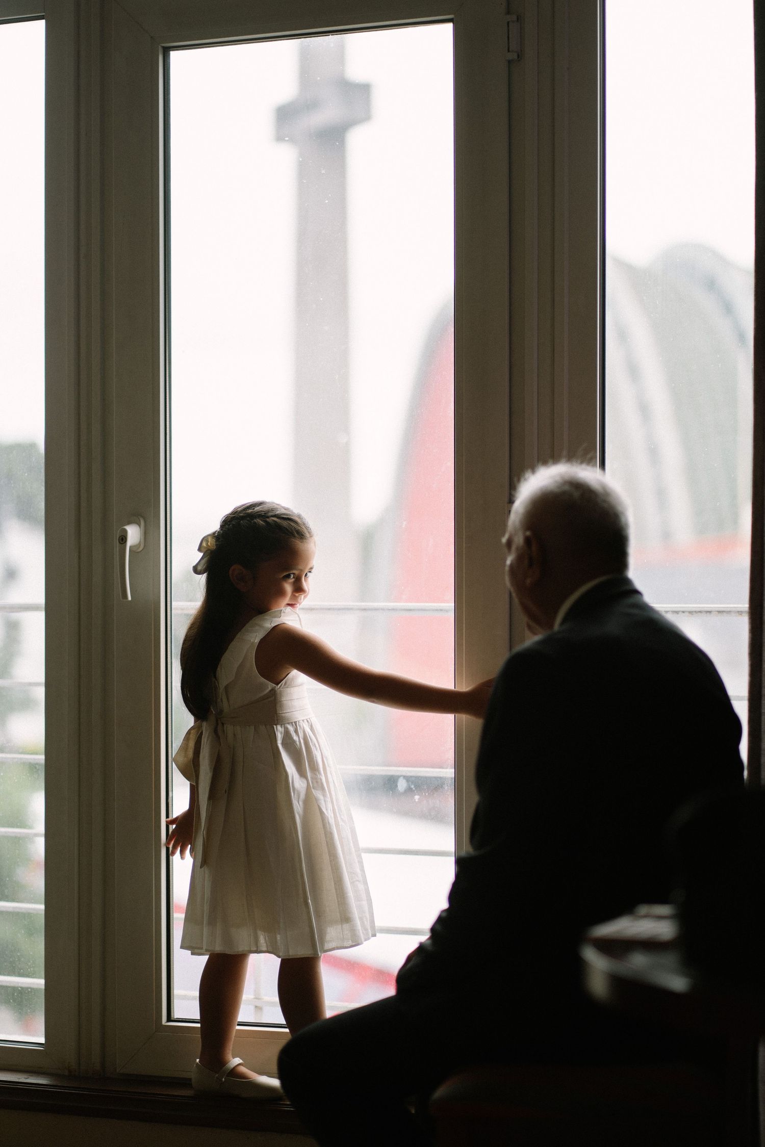 A silhouetted view through a window shows two figures looking out at a tall monument or tower in the distance.