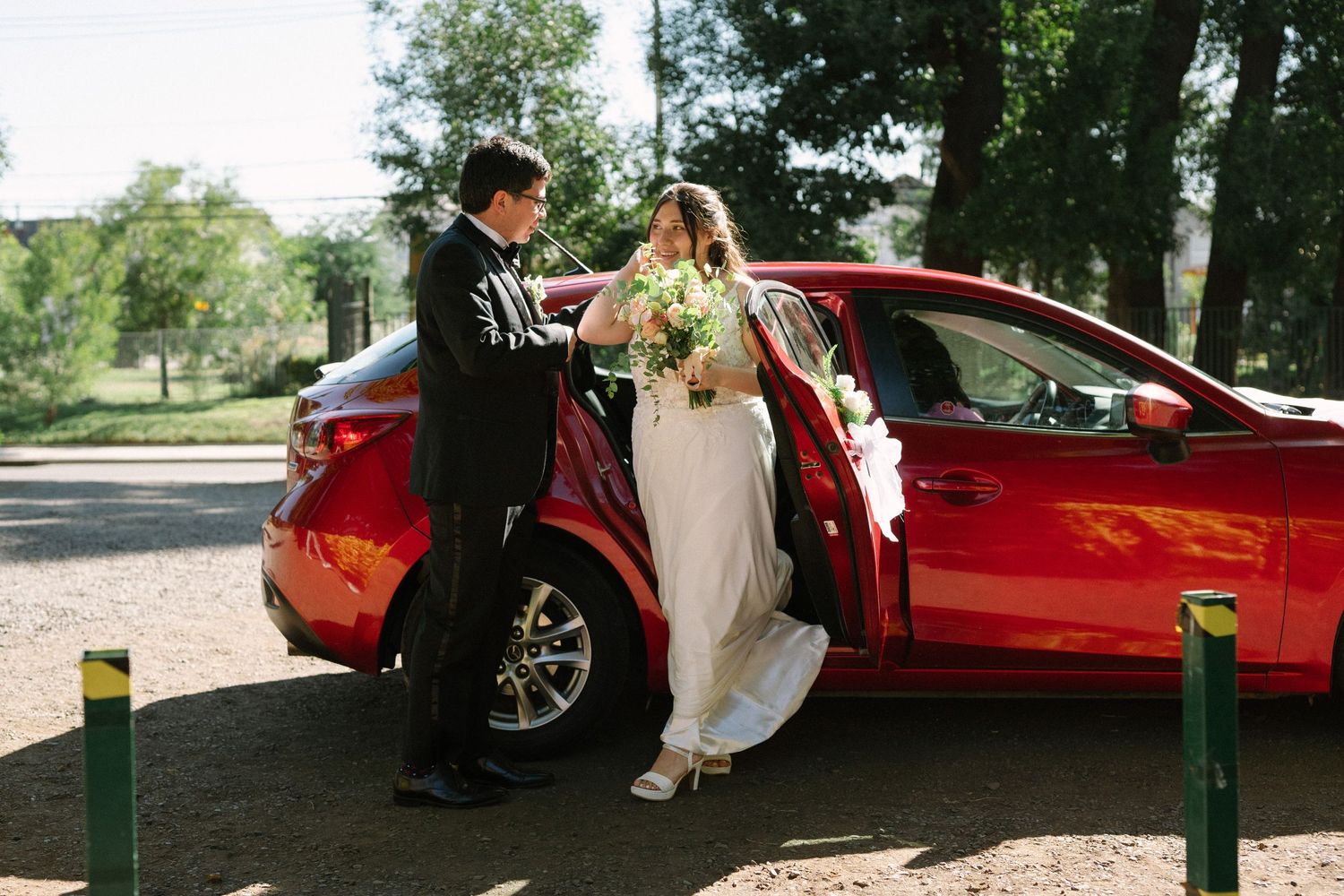 Newlyweds share a moment near a red car decorated for their wedding day.