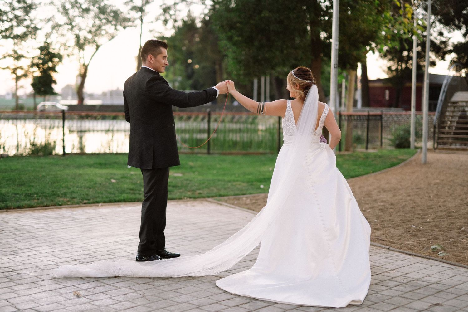 Couple in wedding attire dancing and holding hands on a brick pathway at dusk.