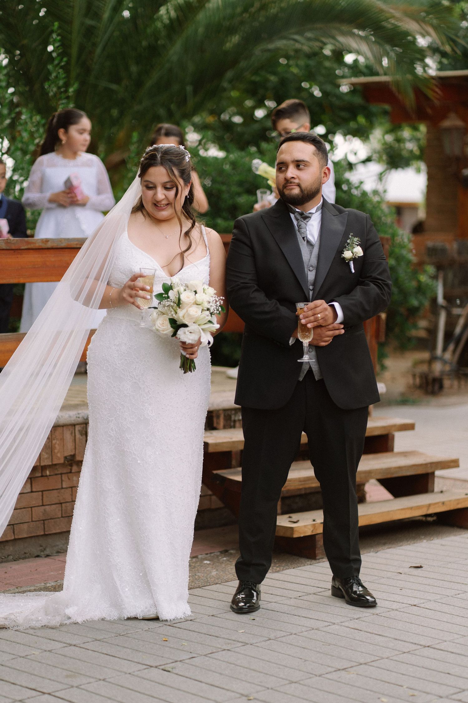 Bride in white gown holding bouquet walks with groom in black suit during outdoor wedding ceremony.