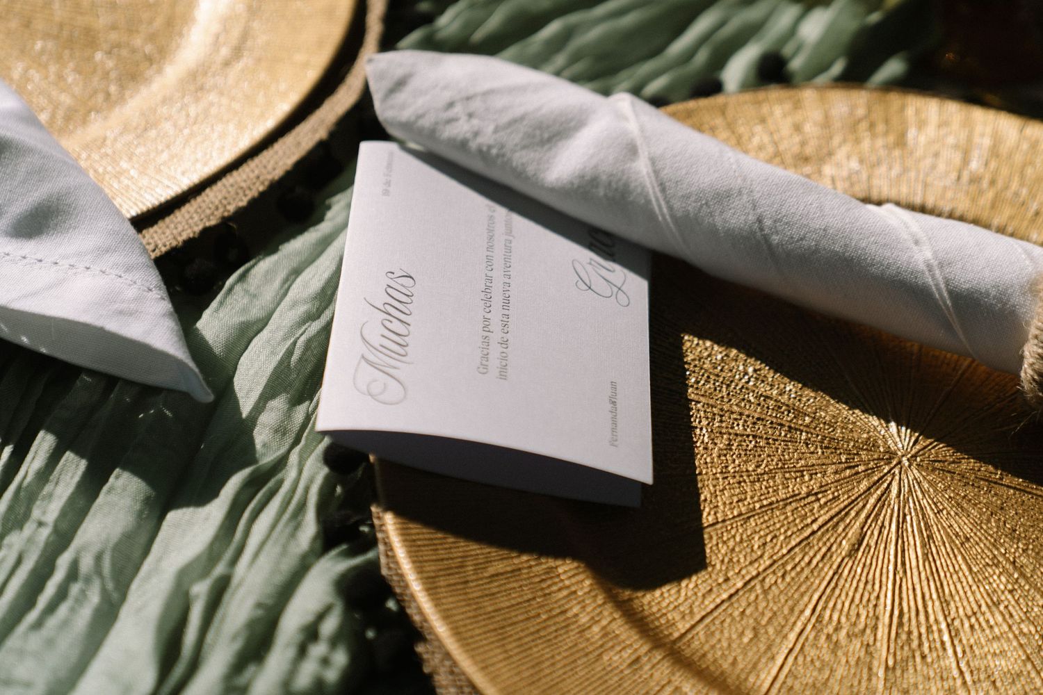 Gold charger plate with elegant place card and sage green napkin at a wedding reception table setting.