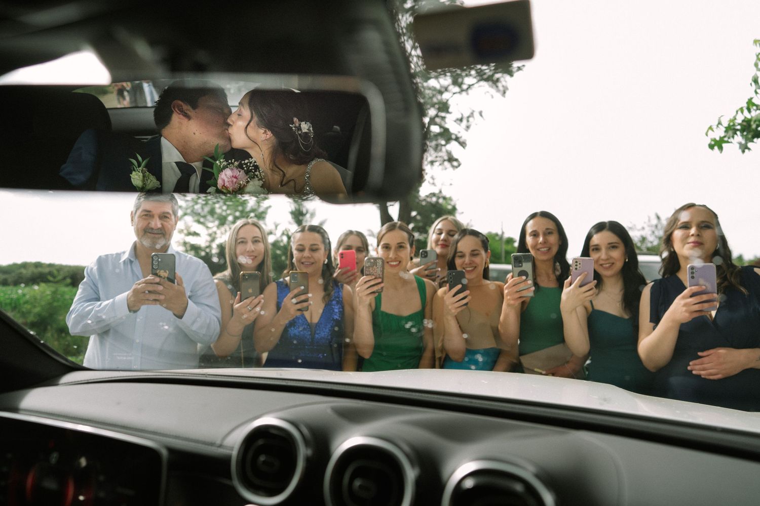 Wedding party poses behind car window with drinks for celebratory photo.