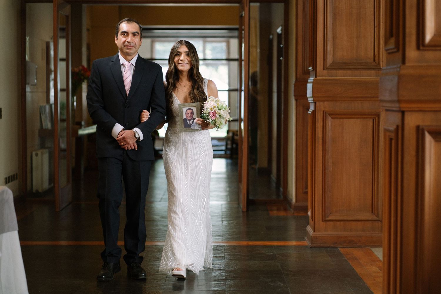 A couple walks down an elegant hallway during a formal ceremony.