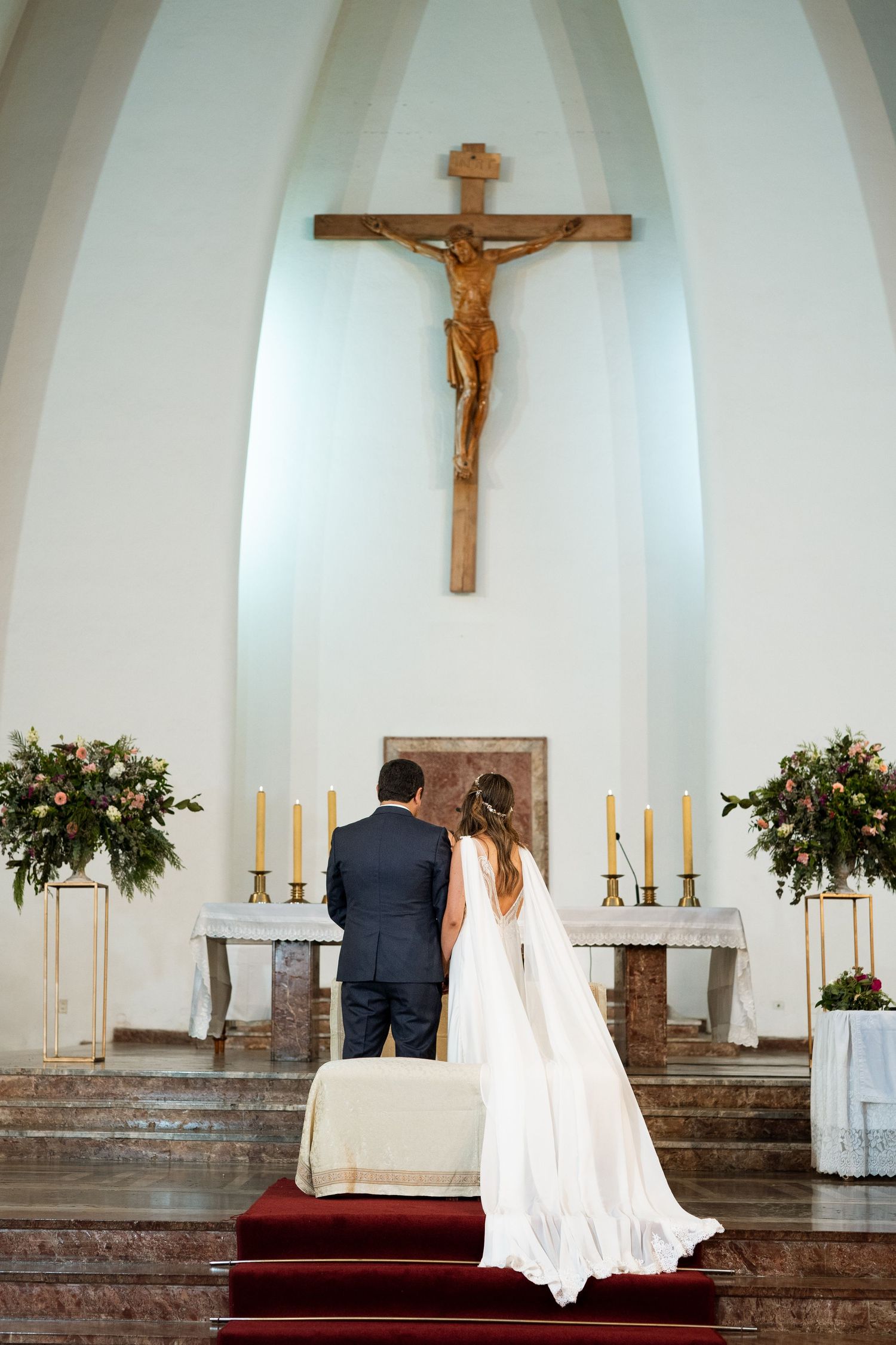 Wedding ceremony at church altar with crucifix, candles and floral decorations.